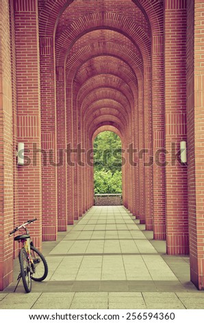 Bike Leaning on the front part of an arch corridor. There are two white street lamps fixed on the arches. The arches are dark-red, and the bike is silver with yellow and pink colors and a black seat.