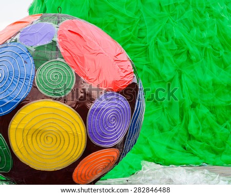 Colorful ball decoration against green plastic net. The ball was made of colorful, glossy plastic fabric and steel wire. There are red, green, purple, yellow and blue colors in the image.