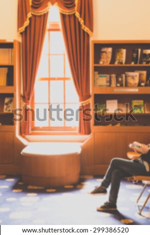 De focused/Blurred image of a girl reading a book by a sunlit window.  The girl wearing jeans and sneakers.