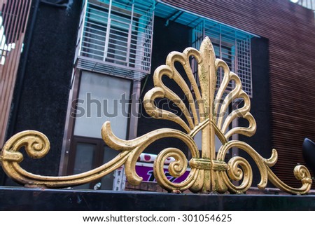 Wrought iron railing in symmetrical pattern on top of a gate. Golden color.