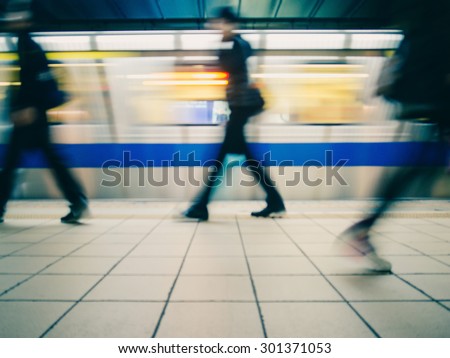 Subway train leaving station. People coming to or leaving the platform. Motion blur. City life. Slightly blue-toned.