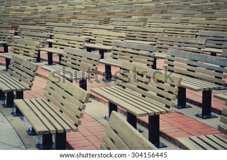 Rows of brown wooden benches in the park.  Benches arranged in curved lines. Soft focus.