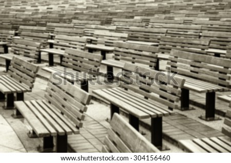 De focused/Blurred, Sepia toned image of rows of wooden benches in the park.  Benches arranged in curved lines.