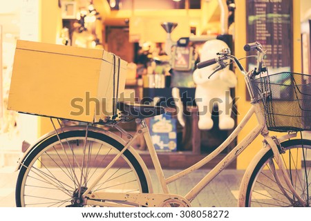 White bicycle with a yellow box in back seat parked in front of a cafe. Retro effect.