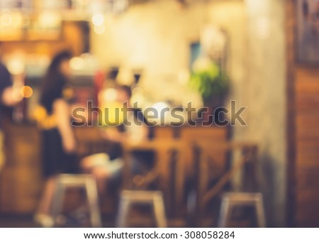 De focused/Blur image of a girl standing and a boy sitting in front of a open cafe. Blurred people in cafe. Retro effect.