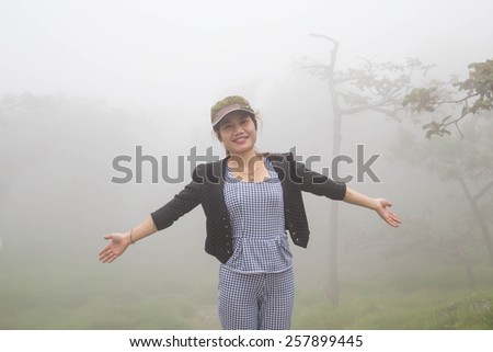 A woman standing on a mountain in the morning with fog.
