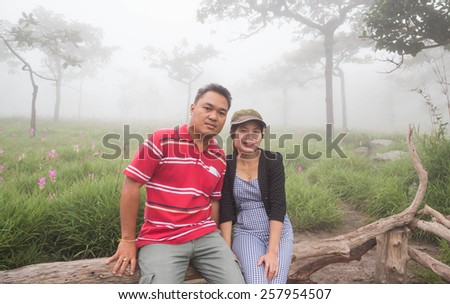 Man and woman sit on the mountain in the morning fog.