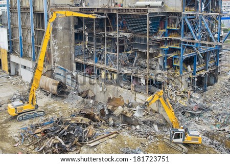 Excavators working in a demolition site in front of a  big metal construction destroyed