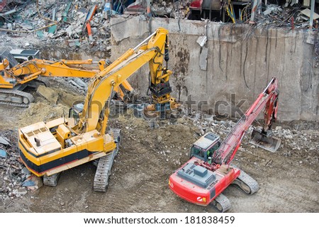 Excavators working in a demolition site in front of a  big metal construction destroyed