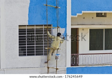 Indian man coloring blue color on wall hanging on a rope ladder