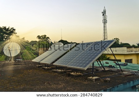 Set of small solar panels on the roof along with dish antenna and mobile phone tower at the background