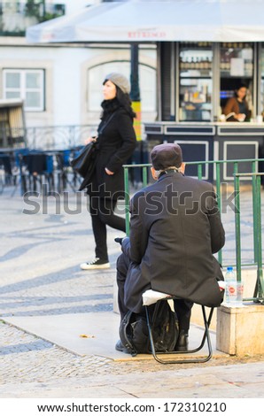 LISBON, PORTUGAL - DECEMBER 5, 2013: Unidentified woman, passes indifferent to a homeless begging on the streets of Lisbon.