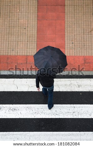 Pontevedra, SPAIN - MARCH 2, 2014: A man with umbrella crossing a crosswalk, on a day of heavy rain in the city of Pontevedra.