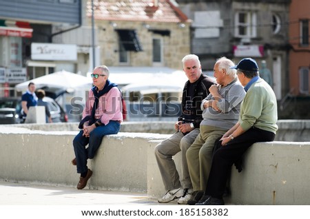 SANXENXO, SPAIN - MARCH 9, 2014: A group of men chatting and sunbathing in Silgar urban beach in the tourist region of Rias Baixas in Galicia.