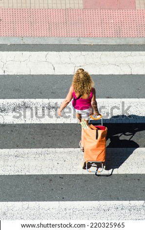 PONTEVEDRA, SPAIN - JUNE 13, 2014: A young woman carrying a shopping cart, it passes over a pedestrian crossing.