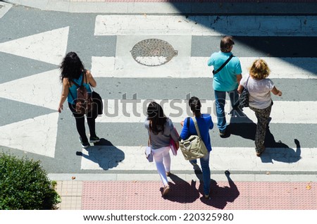 PONTEVEDRA, SPAIN - JUNE 13, 2014: Several people go through a crosswalk, casting its shadow on the pavement.