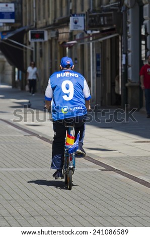 PONTEVEDRA, SPAIN - JULY 25, 2014: A man riding a bicycle wearing a football shirt and carrying a Spanish flag on the back.
