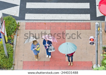 PONTEVEDRA, SPAIN - AUGUST 9, 2014: A group of people with umbrellas, waiting at a crosswalk for the light to turn green.