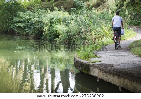 TOULOUSE, FRANCE - OCTOBER 4, 2014: A man rides a bicycle through one of the margins of a navigable river, a tributary of the Garonne river.