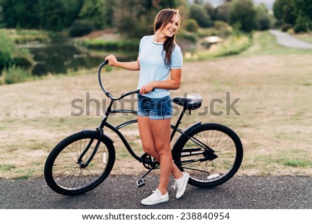 Portrait of Attractive Young Woman in blue shirt with cool beach cruiser bike looking away from camera smiling laughing wide