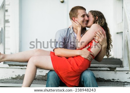 Young Attractive Couple Woman in red dress on lap kissing cheek sitting down on steps