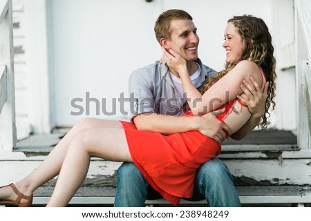 Young Attractive Couple Woman in red dress on lap laughing with each other sitting down on steps
