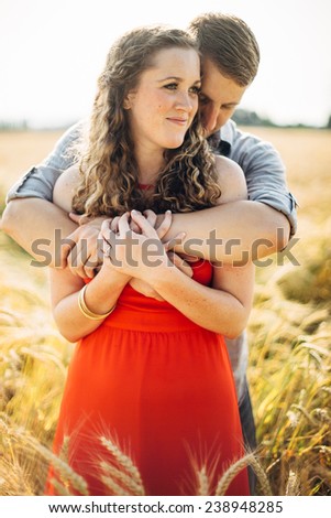 Couple Embracing arms wrapped around female in red dress hugging looking off camera smiling