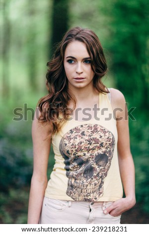 Portrait of Young Attractive Woman in the forest with a skull t-shirt and hand in pocket looking away from camera close up