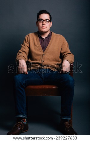 serious portrait of a young man in a sweater vest hands on legs straight on