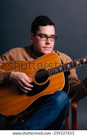 portrait of a young man in a sweater vest playing guitar sitting in chair close up
