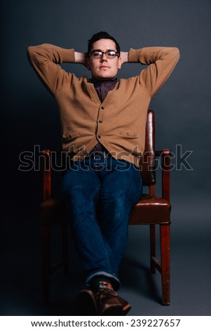 serious portrait of a young man in a sweater vest hands behind head relaxed pose