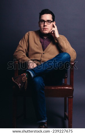 serious portrait of a young man in a sweater vest with fingers on face looking slightly away from camera