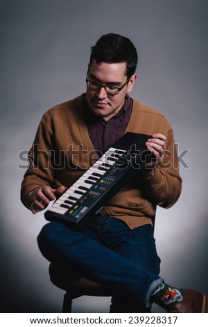portrait of a young man in sweater vest sitting in chair holding a keyboard looking at it close up