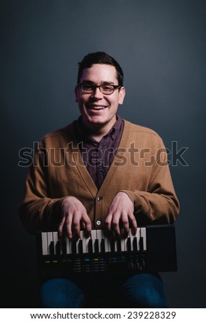 silly portrait of man holding a keyboard on its side with fingers playing keys smiling