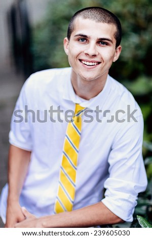 young male student, with tie, smiling, leaning against railing, variation