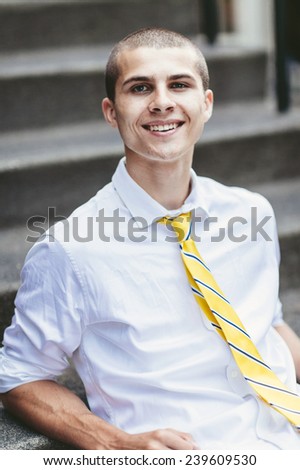 young male student, with tie, smiling, sitting on steps leaning back