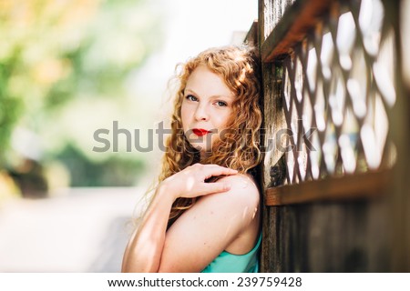 attractive young red head leaning against fence looking at camera slight smile, arm on shoulder