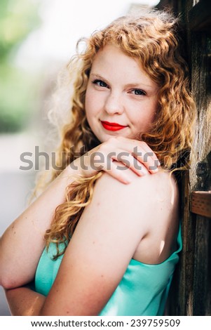 attractive young red head leaning against fence looking at camera slight smile, hugging herself