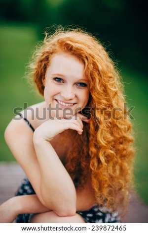 Attractive Young Female Redhead, smiling, hand under chin, sitting on table close up