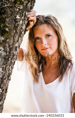 Beautiful Blonde Young Woman arm on tree serious vertical