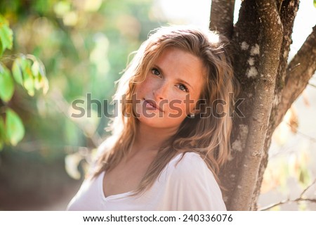 Beautiful Blonde Young Woman leaning on tree zoom