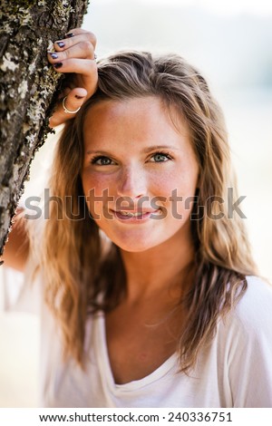 Beautiful Blonde Young Woman head on tree slight smile