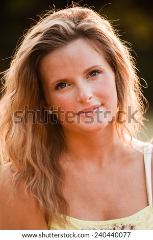 Beautiful Blonde Young Woman in sunset meadow summer day hand on arm slight smile vertical