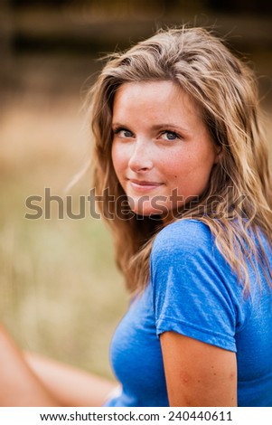 Beautiful Blonde Young Woman blue shirt on ground slight smile behind closer