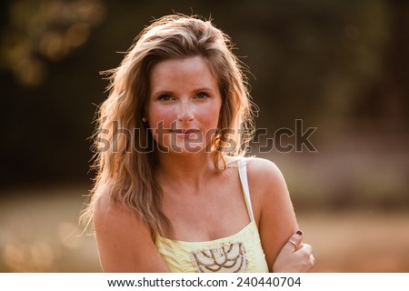 Beautiful Blonde Young Woman in sunset meadow summer day hand on arm slight smile