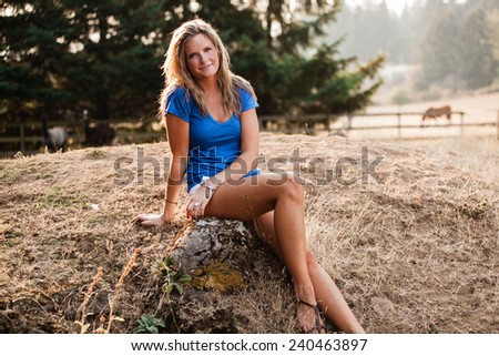 Beautiful Blonde Young Woman in blue shirt sitting on rock in barn area variation