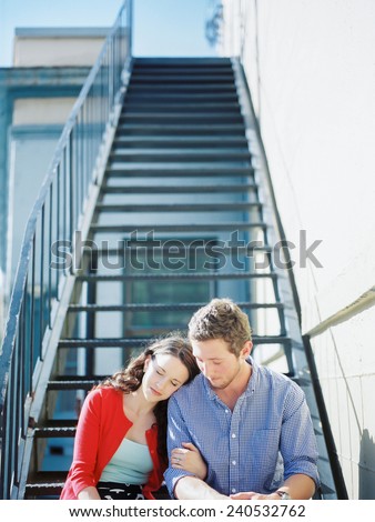 Attractive Young Couple sitting on steps with woman leaning on mans shoulder eyes closed