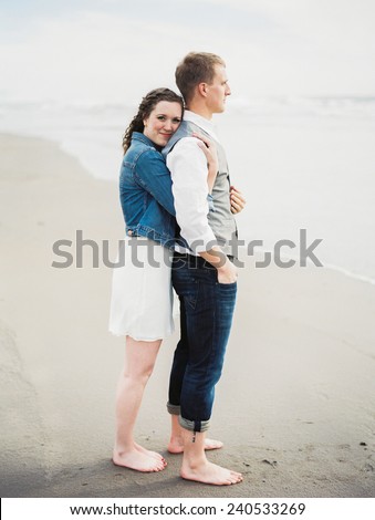 Attractive Young Blond Couple  on beach, woman hugging man from behind, smiling at camera