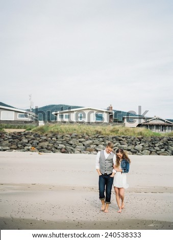 Attractive Young Blond Couple  on beach, walking, with beach homes behind