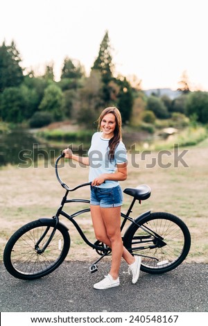 Portrait of Attractive Young Woman in blue shirt with cool beach cruiser bike smiling at camera